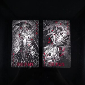 Op de afbeelding: Twee rechthoekige tarotkaarten met zwart-witte illustraties en rode accenten. De linkerkaart toont drie bekers en gevleugelde figuren met de tekst Three of Cups. De rechterkaart toont een groot wiel en bekers met de tekst Eight of Cups.