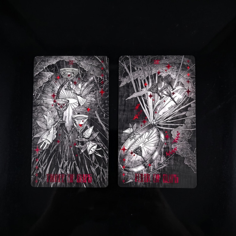 Op de afbeelding: Twee rechthoekige tarotkaarten met zwart-witte illustraties en rode accenten. De linkerkaart toont drie bekers en gevleugelde figuren met de tekst Three of Cups. De rechterkaart toont een groot wiel en bekers met de tekst Eight of Cups.