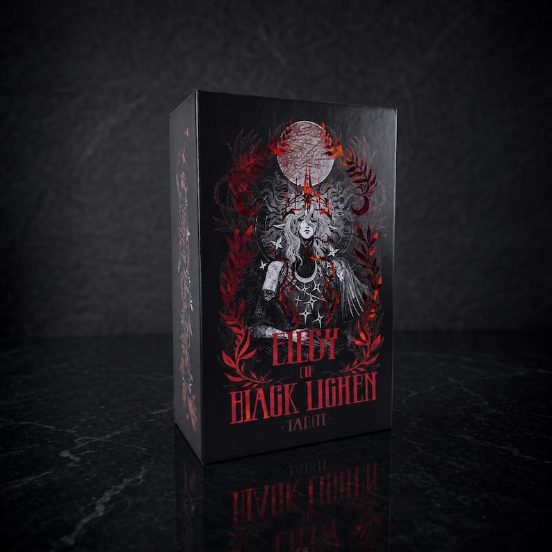 Op de afbeelding: Een zwarte rechthoekige tarotdoos met een centrale illustratie van een figuur met lang haar, een maansikkel en rode bladeren. De tekst Lily of Black Lighen Tarot staat in een opvallend rood lettertype op de donkere achtergrond.