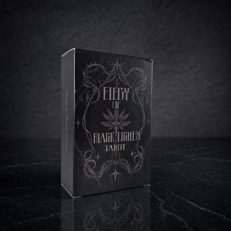 Op de afbeelding: Een zwart rechthoekig tarotdeckdoosje met de witte tekst Elegy of Black Lichen Tarot. Het ontwerp op de voorzijde toont een gestileerde bloem in het midden, omringd door gedetailleerde illustraties van doornige ranken en kleine vierpuntige sterren.