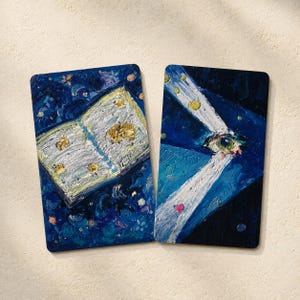 May include: Two rectangular art prints with rounded corners. One depicts an open book with gold accents against a dark blue background. The other shows an eye with light beams, also on a dark blue background.