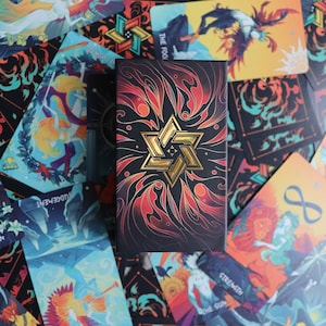 K&ouml;nnte beinhalten: Ein Tarotkartenspiel mit einer schwarzen und goldenen Schachtel. Die Schachtel hat ein goldenes Sternendesign auf einem roten und schwarzen Hintergrund. Die Karten sind um die Schachtel herum verstreut und zeigen verschiedene Bilder von Menschen und Tieren.