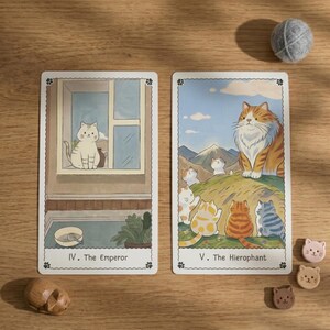 May include: Two rectangular tarot cards featuring cat illustrations. The left card, IV. The Emperor, shows a white cat in a window. The right card, V. The Hierophant, depicts a large orange tabby cat overlooking smaller cats on a grassy hill.