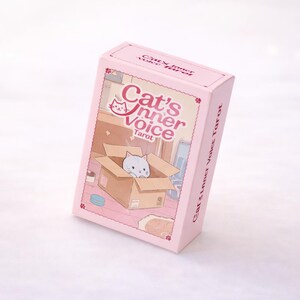 May include: A light pink rectangular tarot card deck box featuring the text Cat's Inner Voice Tarot. The front illustration depicts a small white cat sitting inside a brown cardboard box within a room, with small flower accents on the box corners.