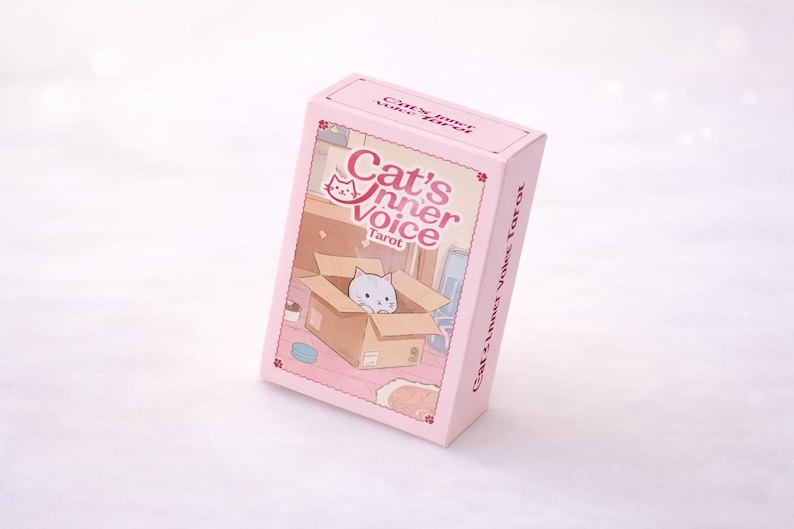 May include: A light pink rectangular tarot card deck box featuring the text Cat's Inner Voice Tarot. The front illustration depicts a small white cat sitting inside a brown cardboard box within a room, with small flower accents on the box corners.