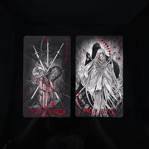 Op de afbeelding: Twee rechthoekige tarotkaarten met zwart-witte illustraties en rode accenten. De linkerkaart toont drie zwaarden die een hart doorboren met de tekst Three of Swords. De rechterkaart toont een figuur met de tekst Two of Swords.