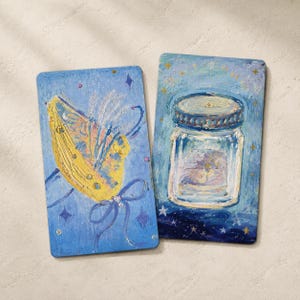 May include: Two rectangular art pieces with a blue background. One features a yellow butterfly with blue accents and a ribbon. The other depicts a glass jar with a silver lid, set against a starry night sky.