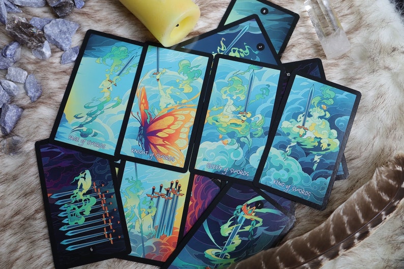 K&ouml;nnte beinhalten: Ein Satz Tarotkarten mit einem Schmetterlingsdesign in Blau-, Gr&uuml;n- und Gelbt&ouml;nen. Die Karten sind mit den Schwertkarten beschriftet, darunter der Ritter der Schwerter, die K&ouml;nigin der Schwerter und der K&ouml;nig der Schwerter.