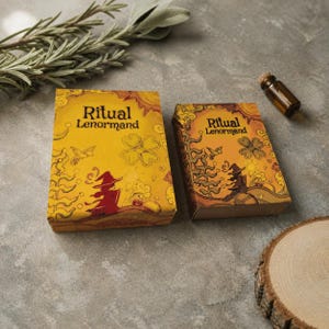 May include: Two rectangular boxes labeled Ritual Lenormand in yellow and orange tones, featuring illustrations of a witch, a bird, and a clover. The boxes are accompanied by a small glass vial and a sprig of rosemary on a gray surface.