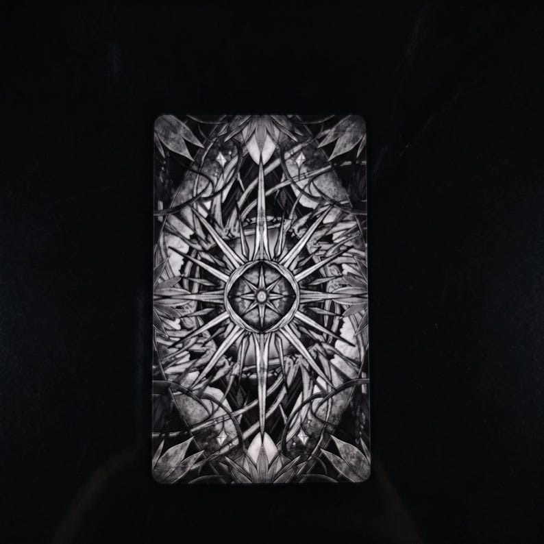Op de afbeelding: Een rechthoekige tarotkaart met een zwart-wit symmetrisch ontwerp. Het midden toont een stervormig patroon met vele punten, omringd door complexe, vloeiende botanische motieven en bladvormige figuren die naar de randen toe uitlopen.