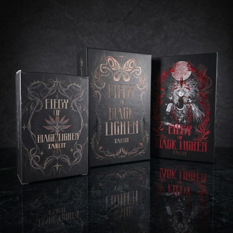 Op de afbeelding: Drie zwarte rechthoekige tarotkaarten-doosjes met de titel Elegy of Black Lighen. De doosjes bevatten gedetailleerde goud- en roodfolie-illustraties van vlinders, doornige ranken en een centrale figuur met een kroon onder een grote maan.