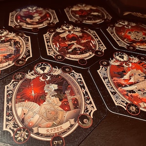 May include: A set of tarot cards with intricate gold and black designs. The cards feature illustrations of a house, clouds, a ship, and a rider on horseback. The cards are set against a dark red background.