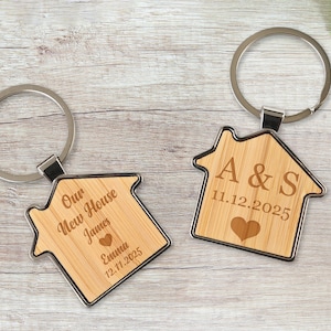 May include: Two wooden house-shaped keyrings with silver key rings. One keyring says "Our New House James Emma 12.11.2025" and the other says "A&S 11.12.2025".