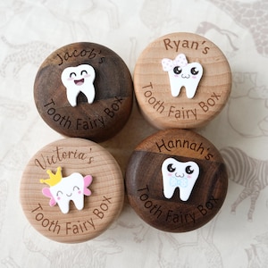May include: Four wooden tooth fairy boxes with personalized names and cute tooth designs. Each box is round with a two-tone wood finish and features a smiling tooth character. The names "Jacob's", "Ryan's", "Victoria's", and "Hannah's" are engraved.