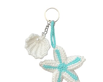 May include: A handmade keychain featuring a white crocheted starfish with turquoise accents and a white seashell with a pearl. The keychain is attached to a silver-colored ring and chain. The design is nautical-themed.