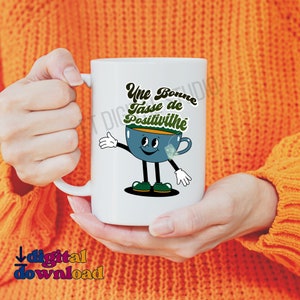 May include: White ceramic mug with a cartoon illustration of a blue teacup with a smiling face and the text "Une Bonne Tasse de Positivité" in green and yellow lettering.