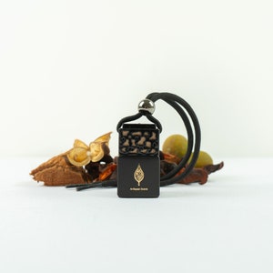 May include: A black and gold diffuser pendant with a black cord. The pendant has a leaf design and the text "Al-Rehab Brands". The diffuser is surrounded by dried botanicals.