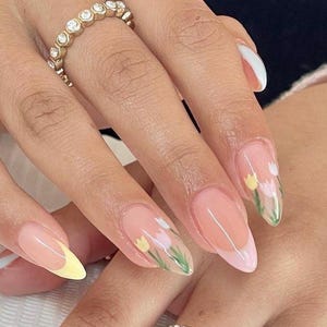 May include: Almond shaped nails with a light pink base and a white tip. The nails are decorated with a floral design of white and yellow tulips with green leaves.