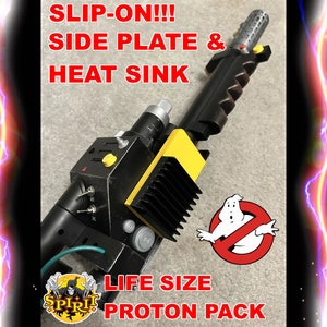 May include: A life-size Proton Pack prop with black, yellow, and silver components. The prop features the text "SLIP-ON!!! SIDE PLATE & HEAT SINK" and "LIFE SIZE PROTON PACK". The Ghostbusters logo is also visible.