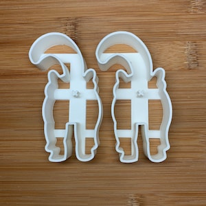 May include: Two white plastic cookie cutters shaped like a pair of cartoon cats standing back to back.