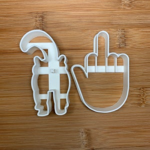 May include: Two white plastic cookie cutters, one shaped like a cat and the other shaped like a hand giving the middle finger.