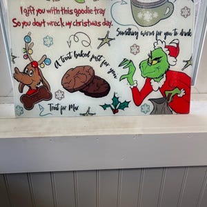 May include: A white glass chopping board with a Grinch and Max the dog design. The board has the text "Dear Mr. Grinch I gift you with this goodie tray So you don't wreck my christmas day. Something warm for you to drink A treat baked just for you Treat for Max"