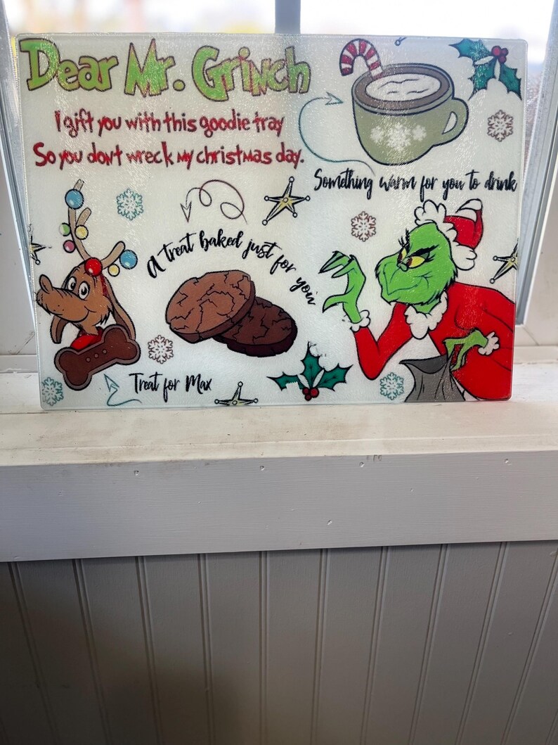 May include: A white glass chopping board with a Grinch and Max the dog design. The board has the text "Dear Mr. Grinch I gift you with this goodie tray So you don't wreck my christmas day. Something warm for you to drink A treat baked just for you Treat for Max"