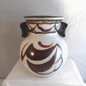May include: A ceramic vase with a rounded body and two dark brown handles. The vase features a white base glaze with hand-painted dark brown abstract curved patterns around the body and a decorative band of brown markings along the wide rim.