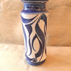 May include: A tall ceramic vase with a white base and a striking blue design. The vase features a series of blue, curved shapes against the white background. The rim and base are also blue, creating a cohesive and artistic look. This decorative vase is suitable for home decor.