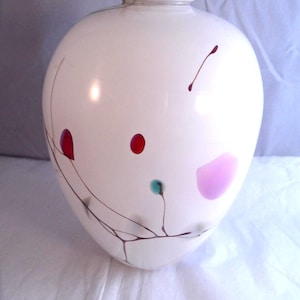 May include: A white, rounded vase with a slender neck. The vase features red, pink, and teal dots and lines. Dark brown lines, possibly hand-painted, create a decorative pattern. The vase is displayed on a white surface.