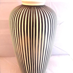 May include: A tall, rounded vase featuring a repeating pattern of vertical black and white stripes. The vessel has a smooth, tapered body that narrows towards the base and a solid white rim at the top opening, creating a high-contrast visual effect.