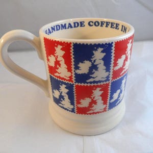 May include: Cream ceramic coffee mug with a white handle. The mug has a repeating pattern of red and blue squares, each with a white outline of the British Isles. The rim of the mug reads "HANDMADE COFFEE IN".