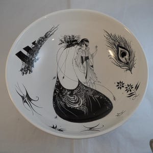 May include: White ceramic serving bowl with black illustrations. The bowl features a central design of two figures in flowing gowns, a peacock feather, and other decorative elements.