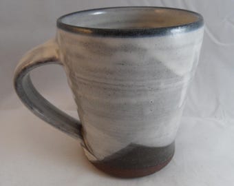 May include: A handmade ceramic mug with a white and gray marbled design. The mug has a dark gray rim and handle, and a brown base. The mug is approximately 5 inches tall.