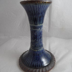 May include: A blue and brown ceramic candle holder with a flared base and a narrow neck. The holder has a textured, striped design.