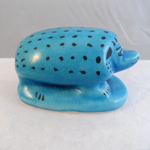 May include: A turquoise ceramic seal sculpture with black spots and a small snout. The base is rounded, and the sculpture has a glossy finish. The seal is a decorative item, likely for display.