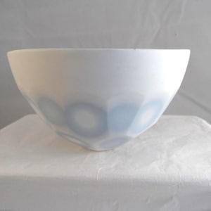 May include: A white ceramic bowl with a light blue circular pattern around the lower section. The bowl has a smooth, glossy finish and a simple, modern design. The bowl is likely used for serving food or as a decorative item.