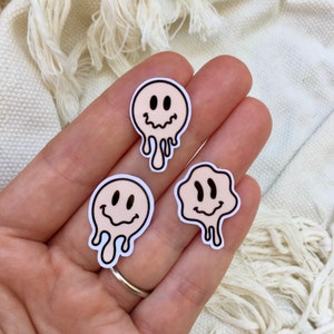Puede incluir: Tres pegatinas de cara sonriente derriti&eacute;ndose en varios tonos de rosa. Las pegatinas tienen contornos negros y est&aacute;n sobre un fondo blanco.