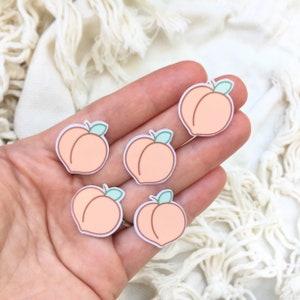 May include: Five peach stickers with green leaves. The stickers are on a hand, and the background is a white fluffy surface.