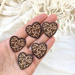 Peut inclure: Cinq ornements en forme de cœur avec un imprimé léopard et des bordures noires. Les cœurs présentent un fond beige avec des taches marron. Les ornements sont présentés sur un fond clair.