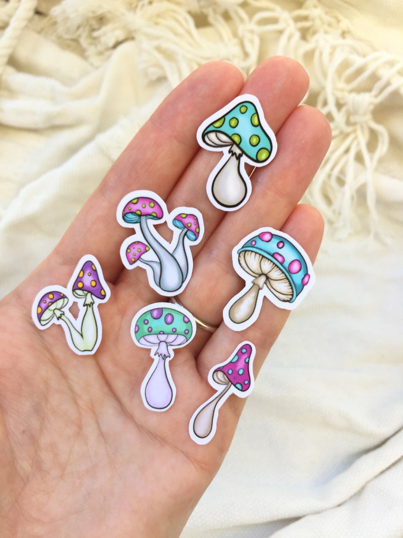 Peut inclure: Un ensemble de sept autocollants de champignons color&eacute;s sur fond blanc. Les champignons ont des chapeaux roses, violets, bleus et verts avec des points blancs. Les tiges sont blanches, bleu clair et vert clair.