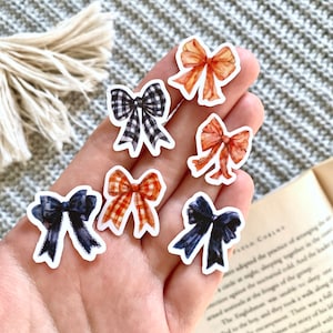 May include: Six watercolor bow stickers in various colors and patterns. The stickers feature a black and white gingham bow, two orange and white gingham bows, two navy blue bows, and one orange bow.