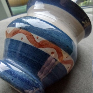 May include: A blue and white ceramic vase with a red and orange design. The vase has a wide mouth and a rounded base.