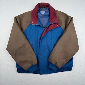 May include: A color-blocked jacket featuring brown sleeves, a blue body, and a maroon collar. The jacket includes a front zipper closure, a snap-button placket, and ribbed cuffs. A label inside the neck displays the text Pendleton and Lobo.