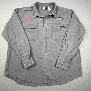 May include: A long-sleeve gray button-down shirt featuring two chest pockets, a collar, and buttoned cuffs. The shirt has the name Mike embroidered in red on the right chest and a small embroidered fish graphic on the left chest.