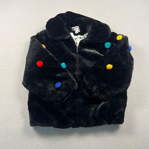 May include: A black faux fur jacket featuring a quilted diamond pattern and a front zipper closure. The jacket is adorned with scattered multi-colored pom-poms in red, yellow, and blue. It includes a white interior lining with a black polka dot print.