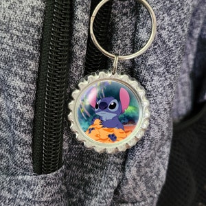 May include: A silver keychain with a round, blue and orange bottle cap charm featuring a cartoon image of Stitch from the Disney movie Lilo & Stitch.