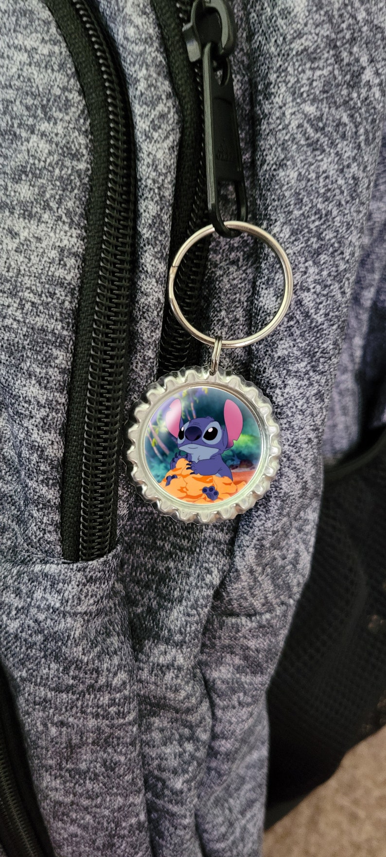May include: A silver keychain with a round, blue and orange bottle cap charm featuring a cartoon image of Stitch from the Disney movie Lilo & Stitch.