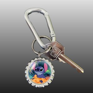 May include: A silver key chain with a blue Stitch character on a bottle cap charm. The key chain has a silver carabiner clip and a silver key ring.