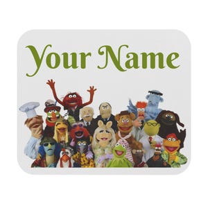 May include: A white mousepad featuring a group of Muppet characters. The text "Your Name" is written in green script at the top. The Muppets include Kermit, Miss Piggy, Fozzie Bear, and others.